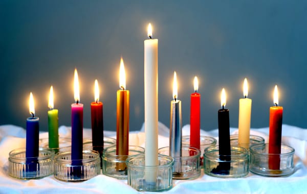 Eleven lit candles of different colours standing in glass holders